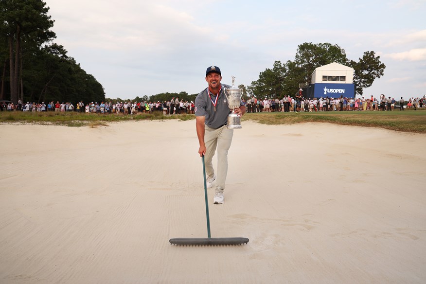 Bryson DeChambeau raking the site of his famous bunker shot on Pinehurst's 18th hole