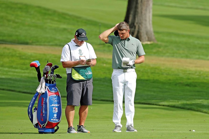 Bryson DeChambeau checks the yardage, weather, moisture, betting odds, soil type and reads Catch 22 before his next shot.